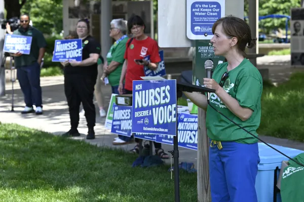 Photo of a nurse speaking at a podium with a sign thaty says "Nurses Deserve a Voice"