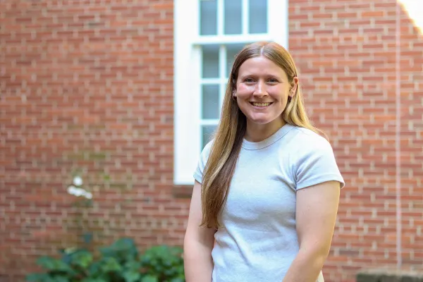 Photo of a white woman with long sandy blonde hair  in light colored teeshirt against brick background