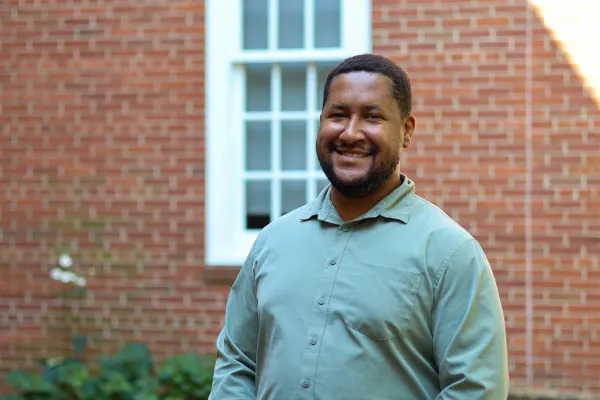 Photo of Black man in light green button down in front of brick wall backdrop