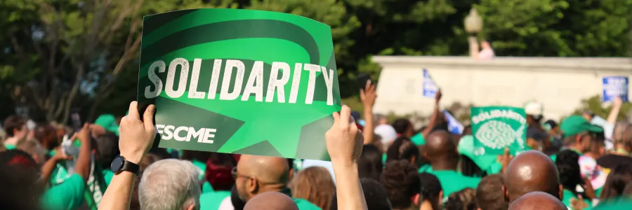 Photo of a rally sign in AFSCME green branding that says SOLIDARITY