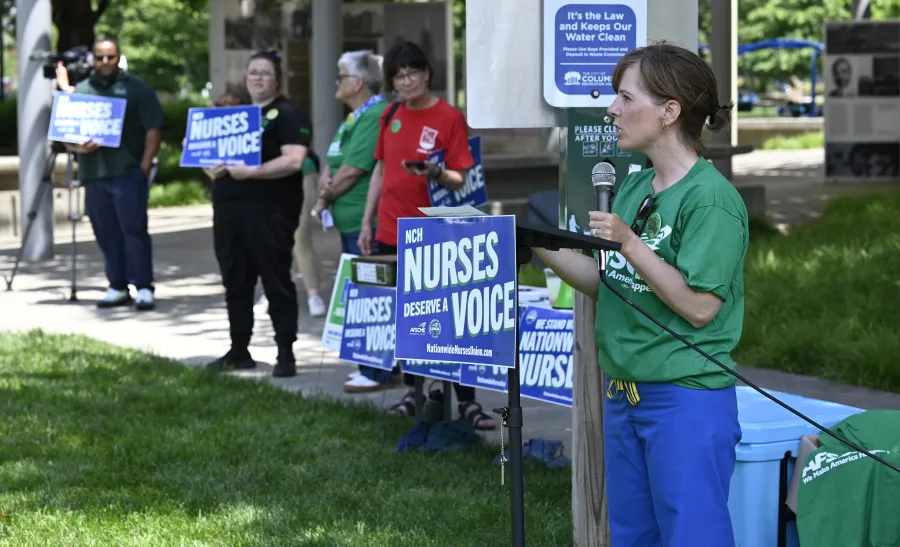 Photo of a nurse speaking at a podium with a sign thaty says "Nurses Deserve a Voice"
