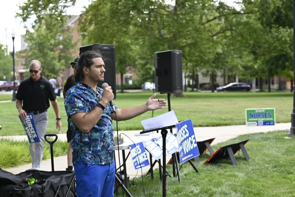Photo of a nurse with Lilo and Stitch scrubs speaking at the rally as a podium with a sign that says "Nurses derve a voice"